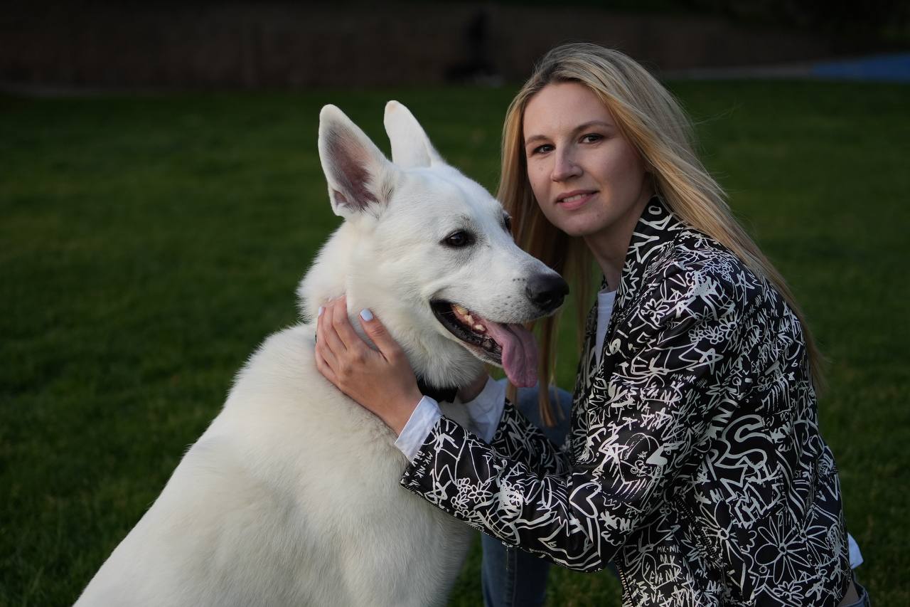 Anastasiia embracing a White Swiss Shepherd on the grass